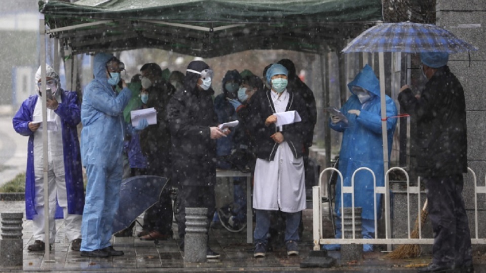 Pracovníci v Číně čekají na pacienty před vstupem do nemocnice.
